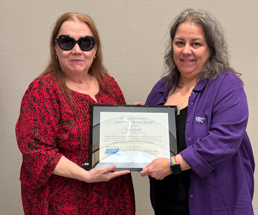 Photo of Kim Charlson dressed in red and dark glasses with Sam Gould dressed in purple holding a the Bay State Council of the Blind's Community Access Award.